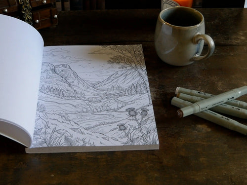 Page de coloriage d'un paysage des Highlands avec château dans la vallée, grand arbre et chardons, à côté d'une tasse en grès et de feutres alcool